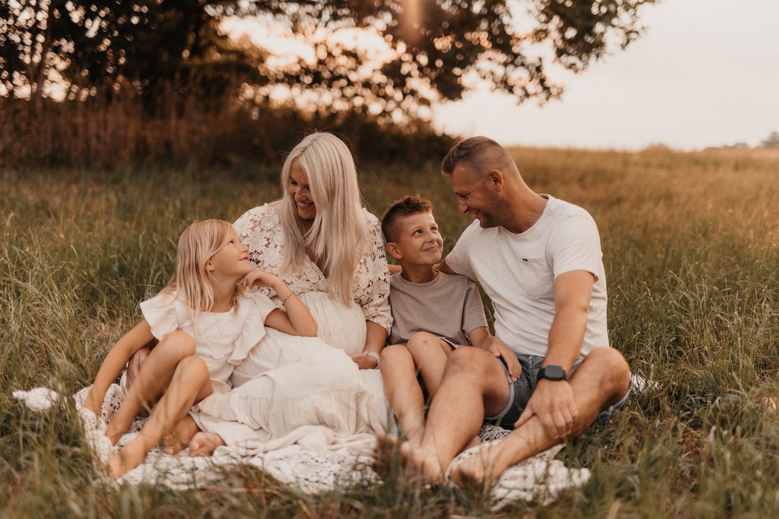 Familie mit zwei Kindern sitzt lachend auf einer Decke im hohen Gras im Abendlicht -- Familienfotografie von Simple Moments