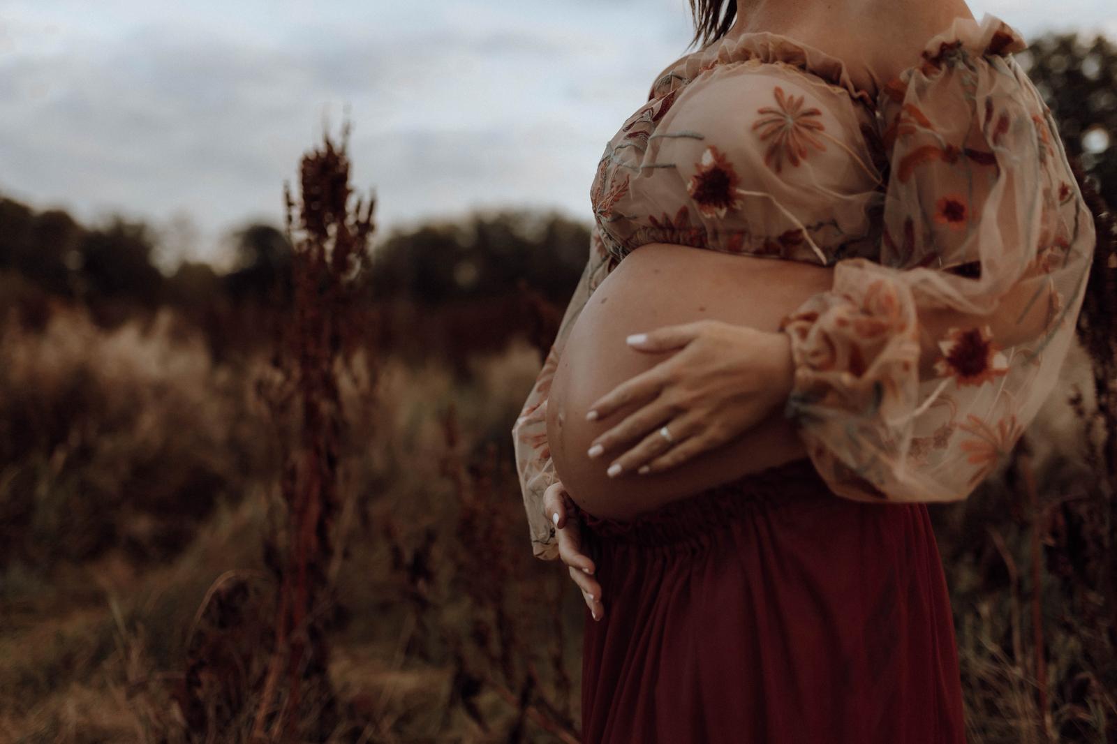 Babybauch-Detail mit floralem Kleid auf herbstlichem Feld