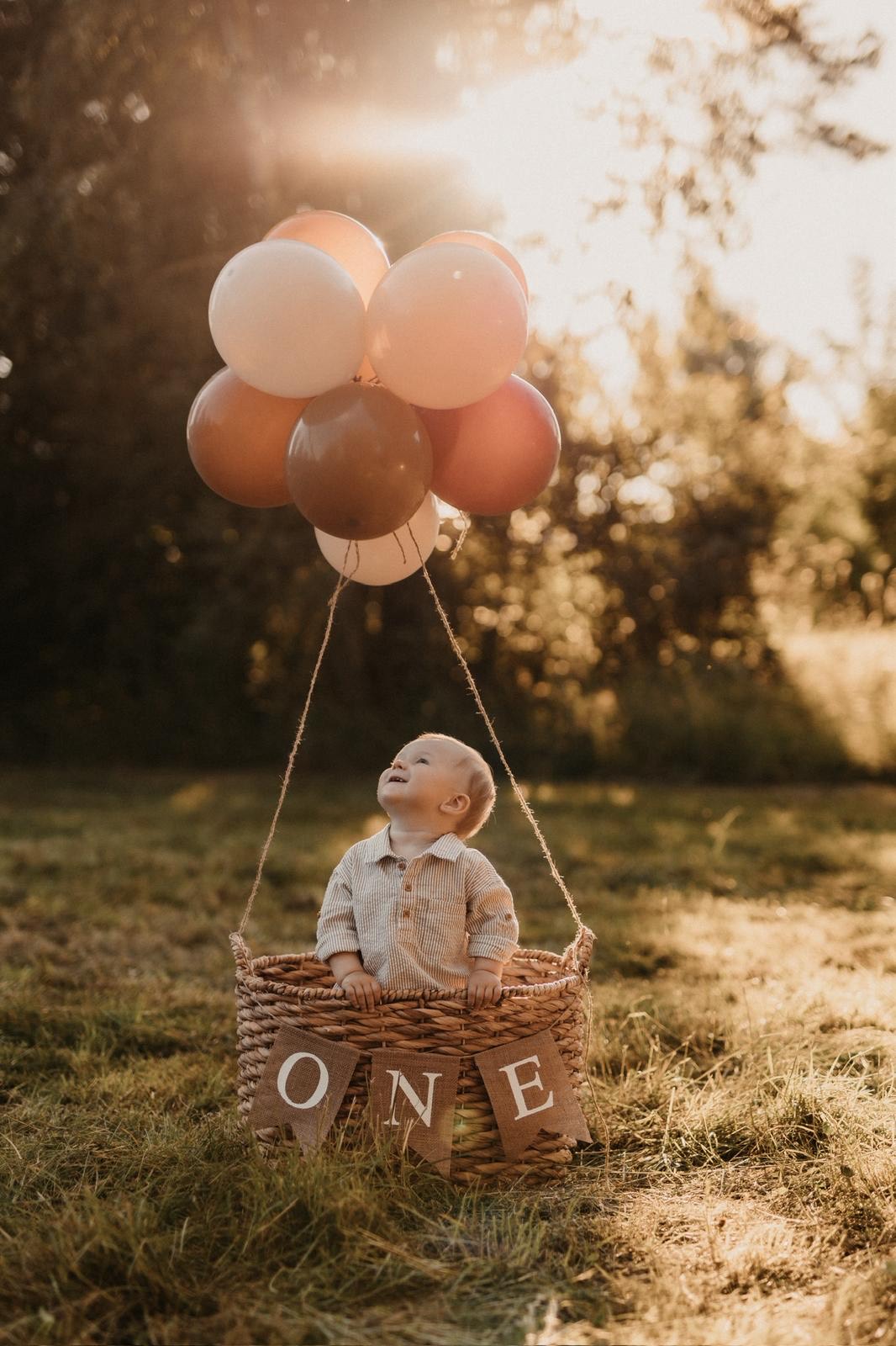 Einjähriger Junge sitzt in einem Korb unter Luftballons und blickt zur ONE-Girlande hoch