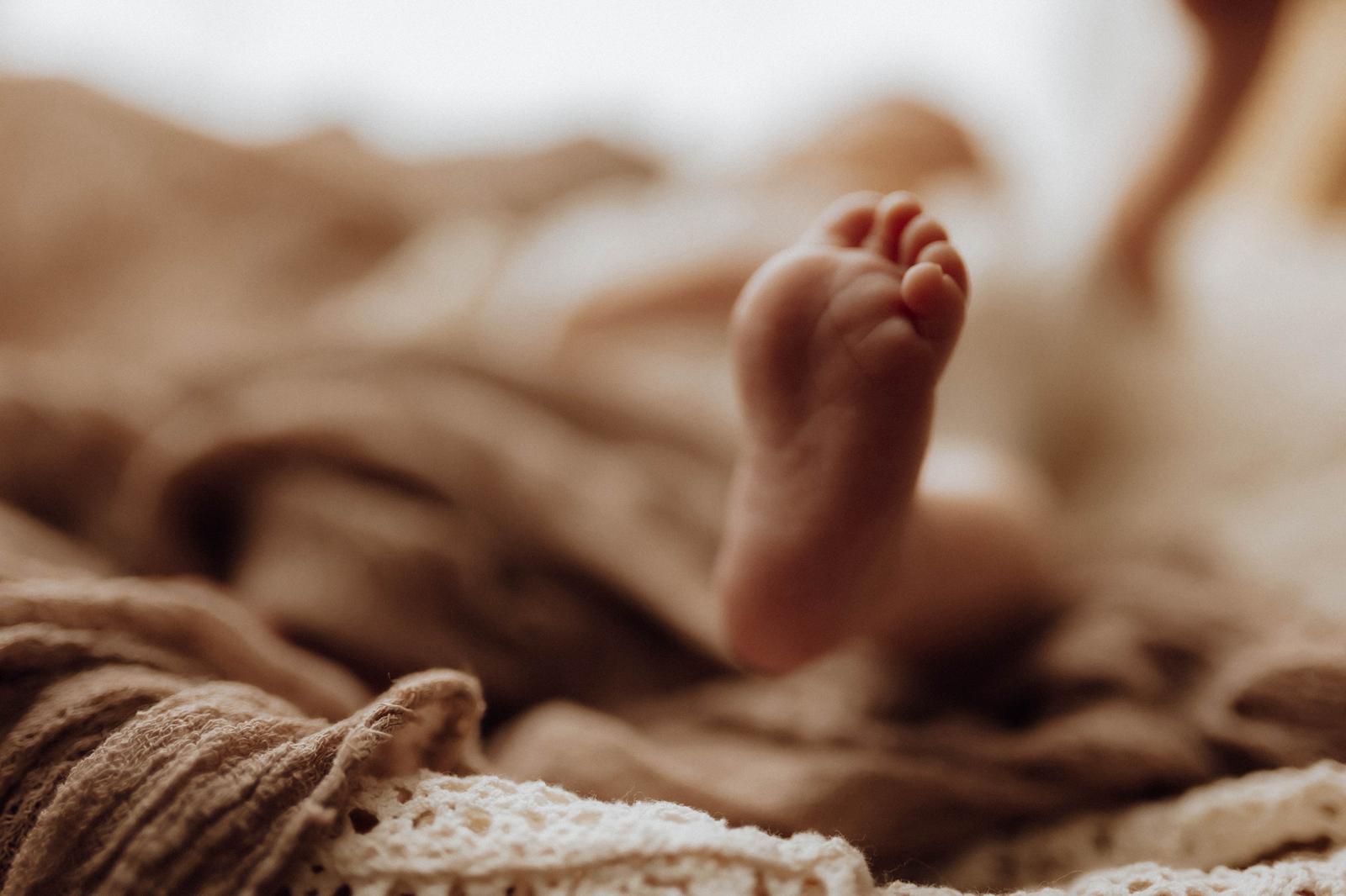 Nahaufnahme eines winzigen Neugeborenen-Füßchens auf weicher Decke