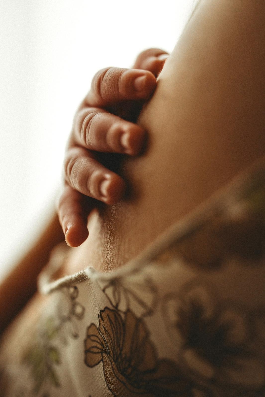 Winzige Neugeborenen-Hand auf der Schulter der Mama im weichen Fensterlicht